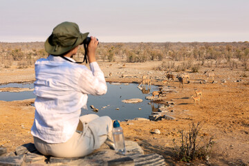 Woman traveler on safari-tour in Africa, watching wild animals with bicolulars and birds in the National park.
