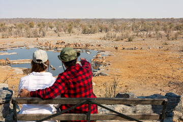 Rear view of young couple observing animals in African savannah, Etosha National Park, Namibia - obrazy, fototapety, plakaty