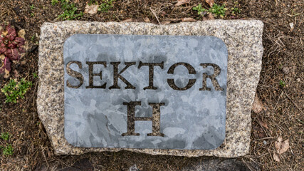 the inscription 'sector h' cut into a gray galvanized metal plate attached to a stone base