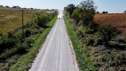 Looking down a gravel road with dust being blown by a vehicle. Path lined by power lines and trees