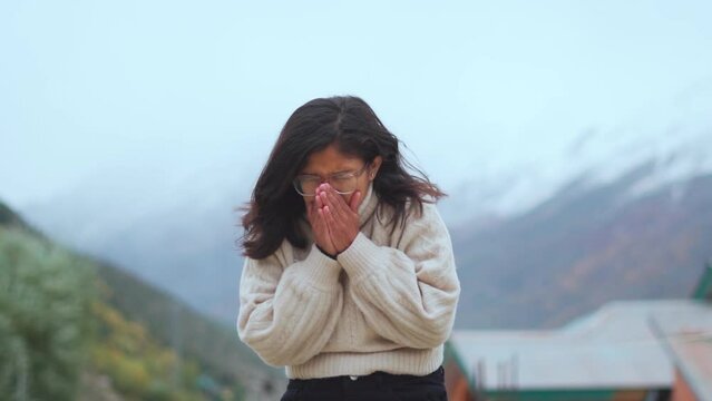 Portrait of Indian girl sneezing, feeling sick and having runny nose. Sick, unwell girl standing against mountains during cold winter in Lahaul, India.Young woman having a flu, sneezing and runny nose