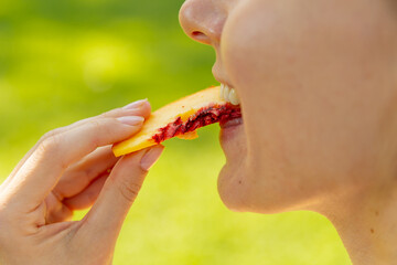 Close up of mouth eating food in public. Woman holding and bites peach or nectarine slices. Picnic concept