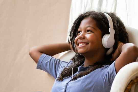 little girl in headphones. a girl sits on a chair and listens to songs in large white headphones near the window