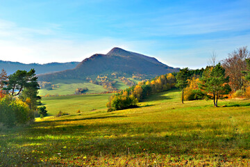 Autumn mountains landscape. Trees on a slope with dry grass and wooded mountains under blue sky with white clouds. View of Mountain Lackowa (997 msl) in Low Beskids. (Beskid Niski) - obrazy, fototapety, plakaty