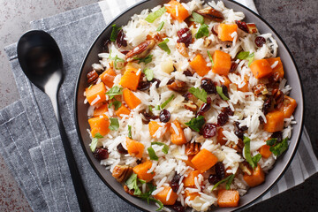Healthy vegetarian pilaf with sweet potatoes, pecans, onions and dried cranberries close-up in a bowl on the table. Horizontal top view from above - obrazy, fototapety, plakaty
