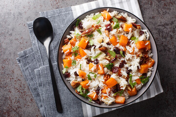 Fragrant rice with sweet potatoes, pecans, onions and dried cranberries close-up in a bowl on the table. Horizontal top view from above - obrazy, fototapety, plakaty