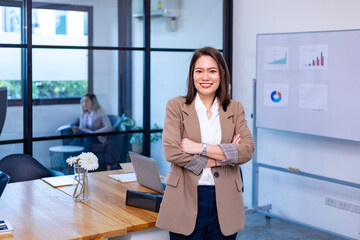 Portrait of Asian business CEO woman is standing crosshand in her office at the table with...