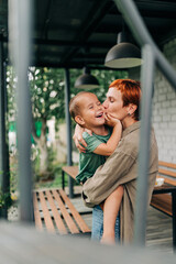 Family mother with her son holding on her hands playful mommy love enjoy time at the terrace redhead woman with short haircut