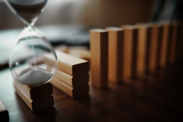 domino effect concept with wooden tiles blocked by hourglass with background