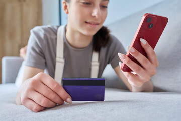 Close-up of credit bank card in hands of young teenage girl with smartphone