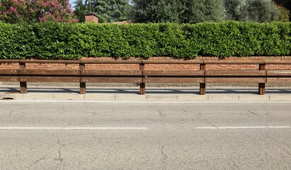 Wooden guardrail on concrete sidewalk. Fence made of brick with hedge on behind and street in front. Suburb background for copy space.