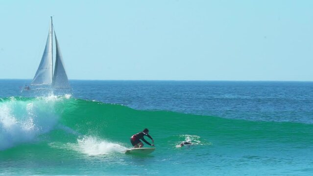 Cinematic pan follow France goofy rider surfing right by sailboat right male surfer huge wave swell morning daytime Hossegor Seignosse Biarritz Spain sunny daylight WSL Quiksilver Roxy Pro in wetsuit