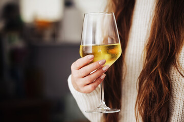 Woman drinking wine. White wine drinking. Wine glass in hand. Girl in woolen sweater. Cozy winter alcohol background. Female hand holding wine glass. Winter season clothing. Long hair shallow depth.