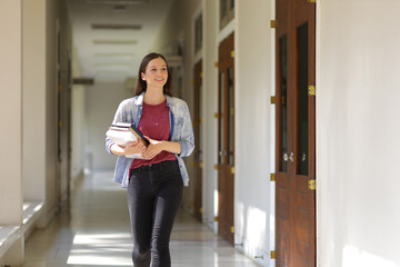 Portrait of a female university student holding a textbook walking on the corridor of the school building. A student holding a book walking into the classroom.