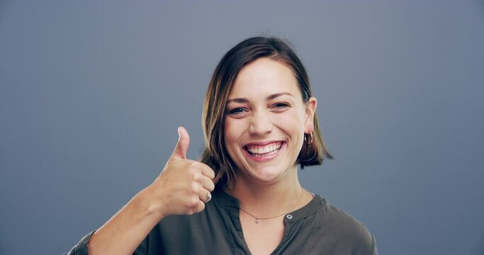 Happy woman, face and thumbs up in winning, good job or success isolated against a studio background. Portrait of young friendly female person smile showing like emoji, yes sign or OK on mockup space