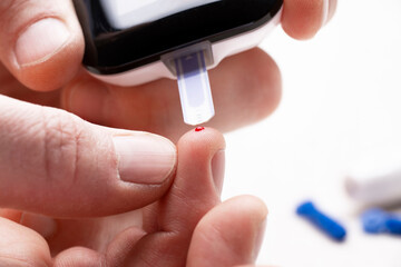 Caucasian fingers with blood drop ready to make home glucose test by glucose meter closeup view....