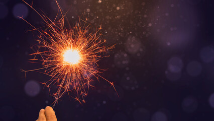 Human hand holding sparkler with colorful blurred light