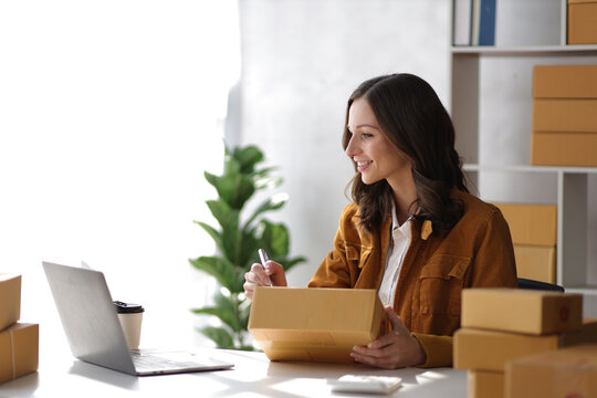 Female entrepreneur starting a small business for online sales working with parcel boxes at home checking orders from the internet preparing for delivery.