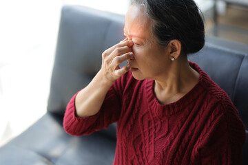 Senior woman sitting on the sofa at home is sick and has a headache.