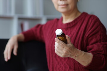 Senior woman at home holding a pill bottle and reading a medicine label.