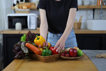 Attractive young woman in the kitchen choosing vegetables in a basket.