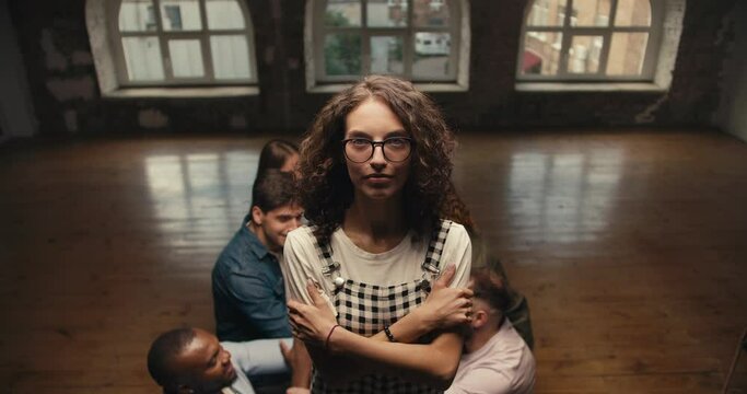 A brunette girl with curly hair wearing glasses in a checkered jumpsuit falls into the arms of her friends in group therapy. Practice trust between people in a group