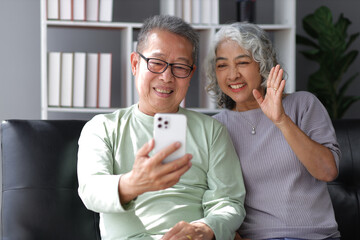 Happy senior couple in retirement at home. Happy grandfather and grandmother talking with grandchildren from home by video call on smartphone.