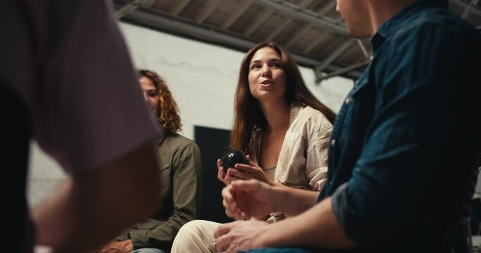 Participants in group therapy pass each other a black ball and express their point of view about the problem in a white brick hall