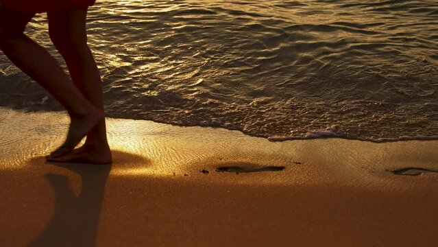 The Girl Walks Along the Seashore, Leaving Footprints in the Sand. Human Footprints On the Sand Disappear Under the Waves Crashing on the Shore. Sunset Time