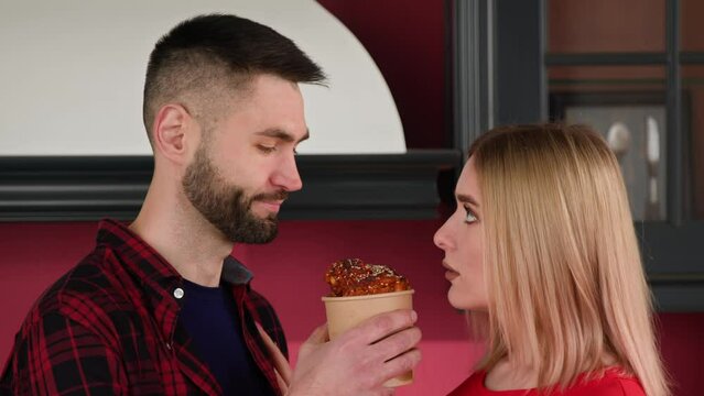 A young blonde woman wants to hug a young brunette man in the home kitchen. Between them is a bucket of chicken wings. The concept of flirting in a relationship and the importance of nutrition.