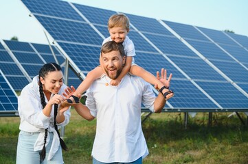 Young family with a small child in her arms on a background of solar panels. A man and a woman look at each other with love. Solar energy concept.