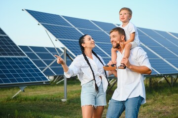 Young family of three is crouching near photovoltaic solar panel, little boy and parents. modern...
