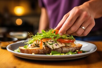 hand placing a piece of fish on an open-faced sandwich - obrazy, fototapety, plakaty