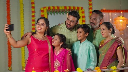 Group of Indian family members making video call on mobile phone for diwali wishes or greetings during festive celebration at home - concept of holiday gathering, traditional culture and communication