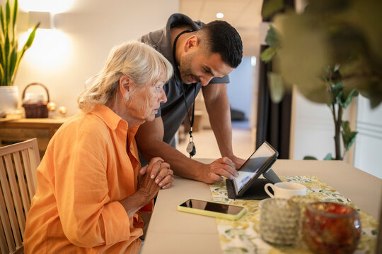 Male nurse assisting senior woman in using digital tablet at nursing home