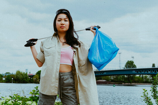 Low angle portrait of confident young woman picking garbage near river