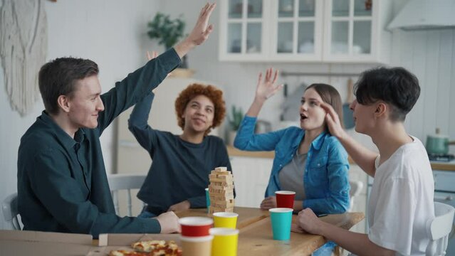 Happy friends giving five each other eating pizza playing tumbling tower sitting on kitchen at home in weekend. Party, people spending time together. Friendship, leisure, support unity togetherness.