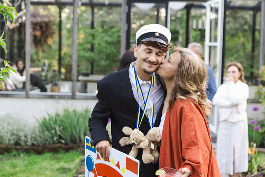 Woman kissing son while standing at back yard during summer party