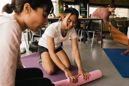 Non-binary business person rolling exercise mat by colleague at office