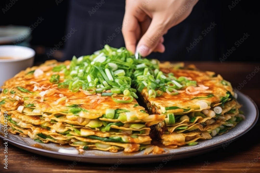 Poster hand garnishing kimchi pancake with chopped green onions