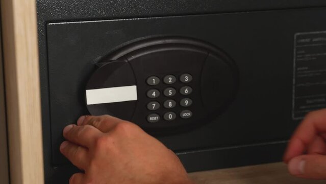 Close-up of a woman's hands typing the password on the door of a metal safe on the door in the hotel and puts money in dollars. Storing money in a hotel.