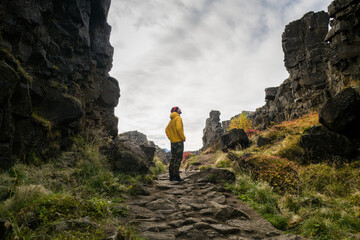 Man wearing a yellow jacket walking between the tectonic plates in the Thingvellir national park - obrazy, fototapety, plakaty