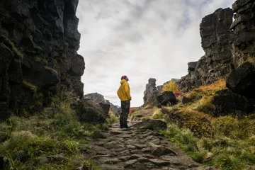 Deurstickers Man wearing a yellow jacket walking between the tectonic plates in the Thingvellir national park © sashapritchard