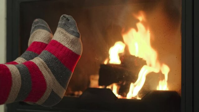 After a hike in the autumn forest, a woman warms her tired feet in old socks by the fireplace, relaxation after hike through the picturesque mountains and an adventure in nature, 4k video in real time