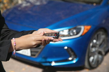 Woman showing car key against the background of a car.