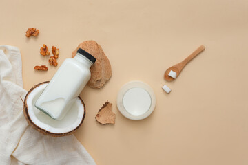 Nut milk bottle with ingredients from fresh coconut and walnuts are placed on a pastel colored background along with some props. Scene for milk advertisements, health and beauty magazines.