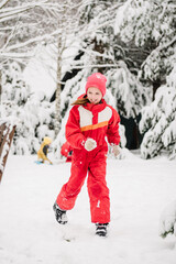 Fototapeta na wymiar Girl running on snow in mountain country in a snowy forest. Little child in winter clothes having fun. Kid wearing warm hat walking in winter park in holidays. Baby plays in among snowdrifts.