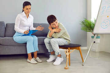 Therapist or psychologist talking to a sad, depressed child. Specialist with a clipboard trying to talk to an upset little school boy. Children's psychology, depression, therapy, mental health concept