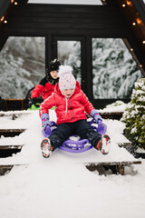Kids on sledge during snowfall on winter day. Happy funny childs ride sled outdoors. Children...