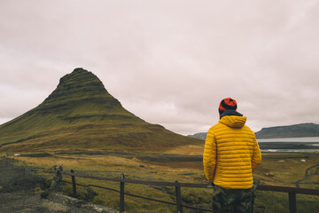 View from behind on man in a yellow jacket overlooking Kirkjufell mountain in Iceland